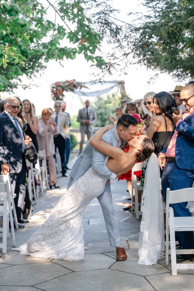 Groom kissing bride in aisle of outdoor wedding at Vine Hill House.
