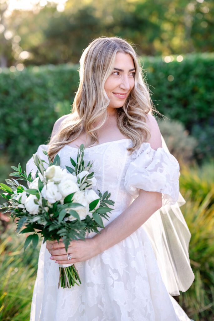 Blonde bride looking behind her while carrying a flower bouquet.