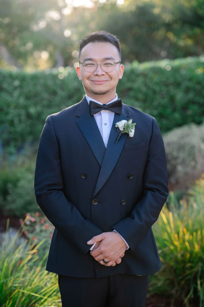 Groom with glasses and bow tie smiling in a tux.