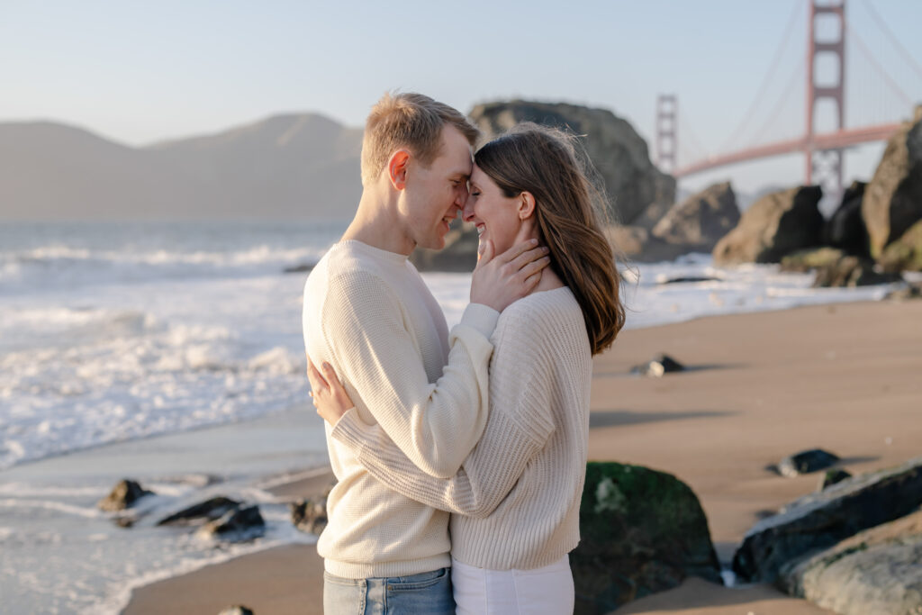 Engaged couple sharing a quiet moment during a Baker Beach proposal in San Francisco, with the Golden Gate Bridge visible in the background.