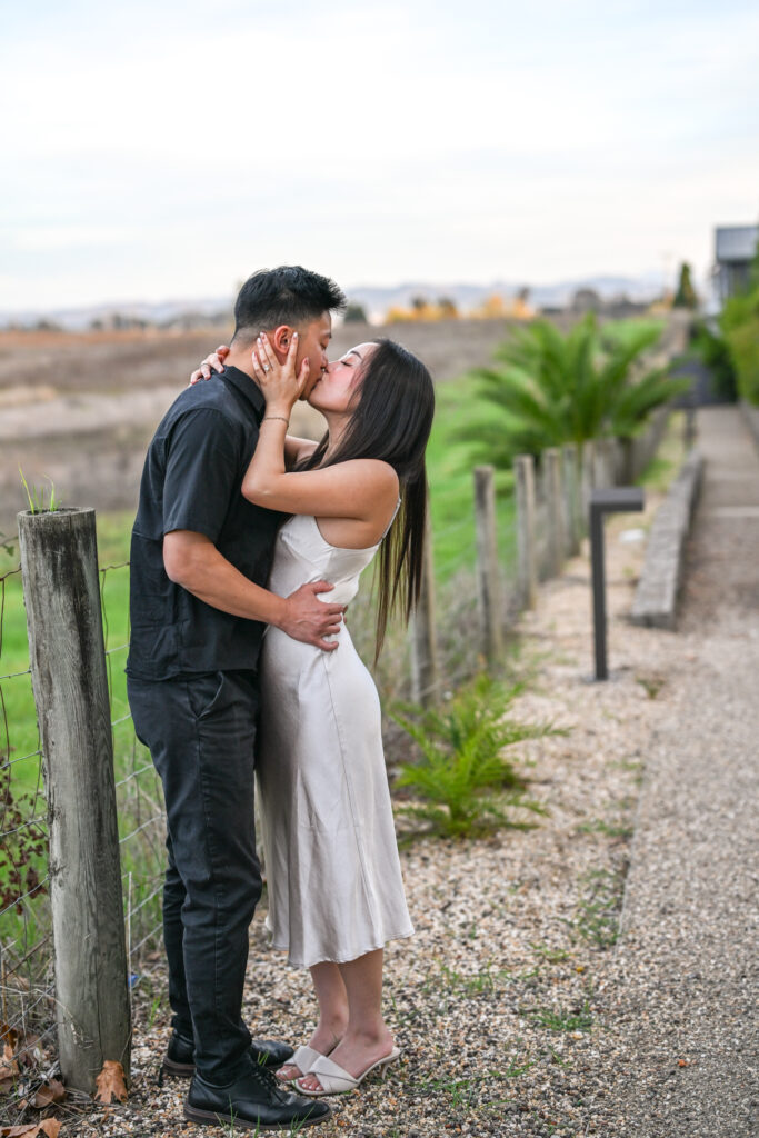 Newly engaged couple embracing and kissing after a proposal at Carneros Resort and Spa, captured along a vineyard path in Napa Valley.