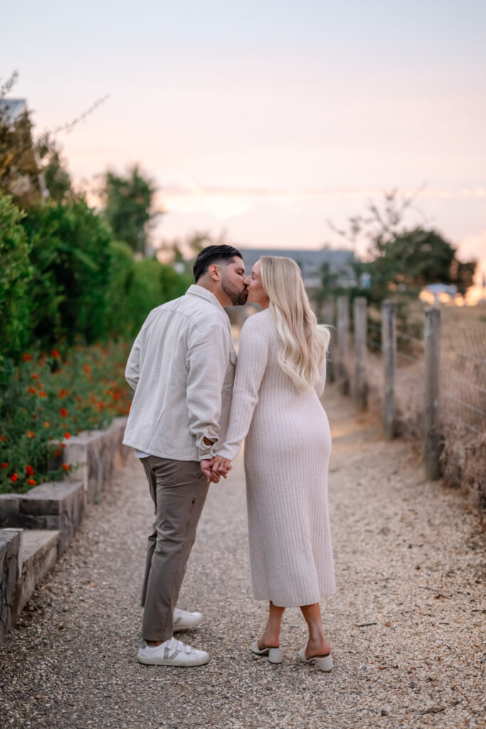 Newly engaged couple holding hands and kissing along a vineyard path at Carneros Resort and Spa in Napa Valley during an engagement session.