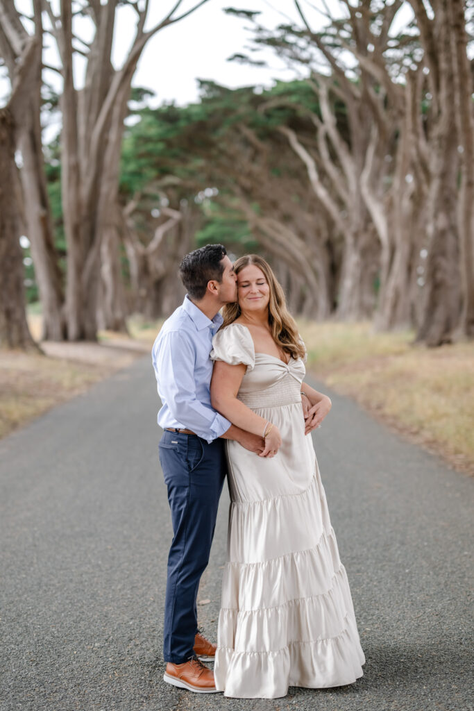 Newly engaged couple standing on a tree lined road near the Marin Headlands, sharing a quiet moment during their proposal session in Marin County, California.