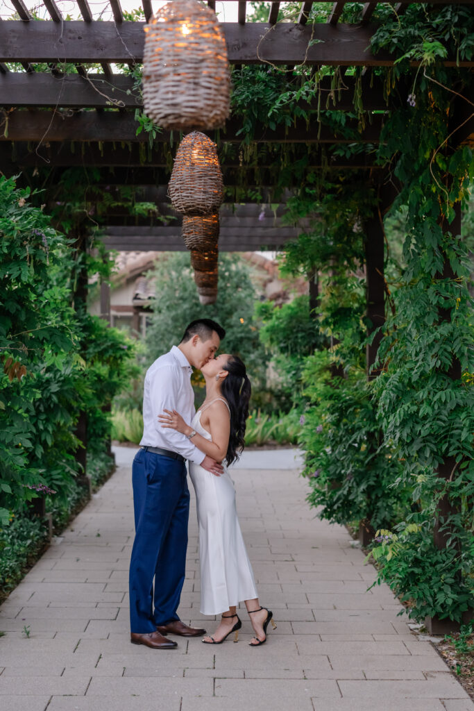Engaged couple kissing beneath a garden pergola at the lodge of Sonoma during a San Francisco proposal, surrounded by greenery and soft evening light.