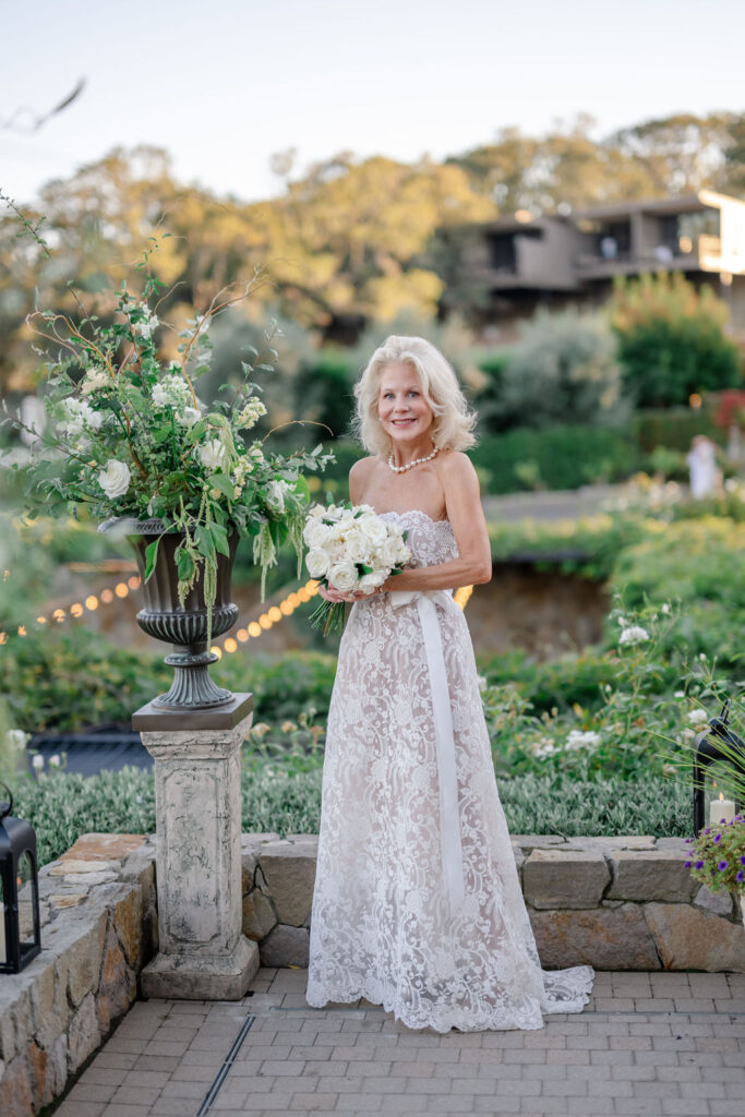 Bride standing on the terrace at Montage Healdsburg holding a white rose bouquet, surrounded by lush greenery and soft evening light.