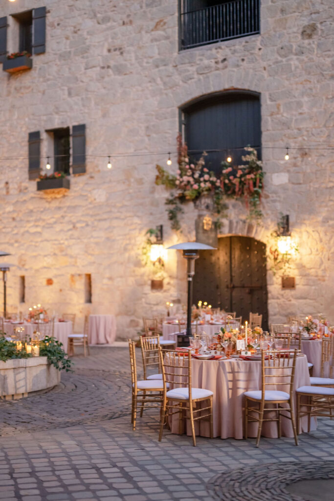 Romantic reception tables in the courtyard of Buena Vista Winery with bistro lights and historic winery building in Sonoma.