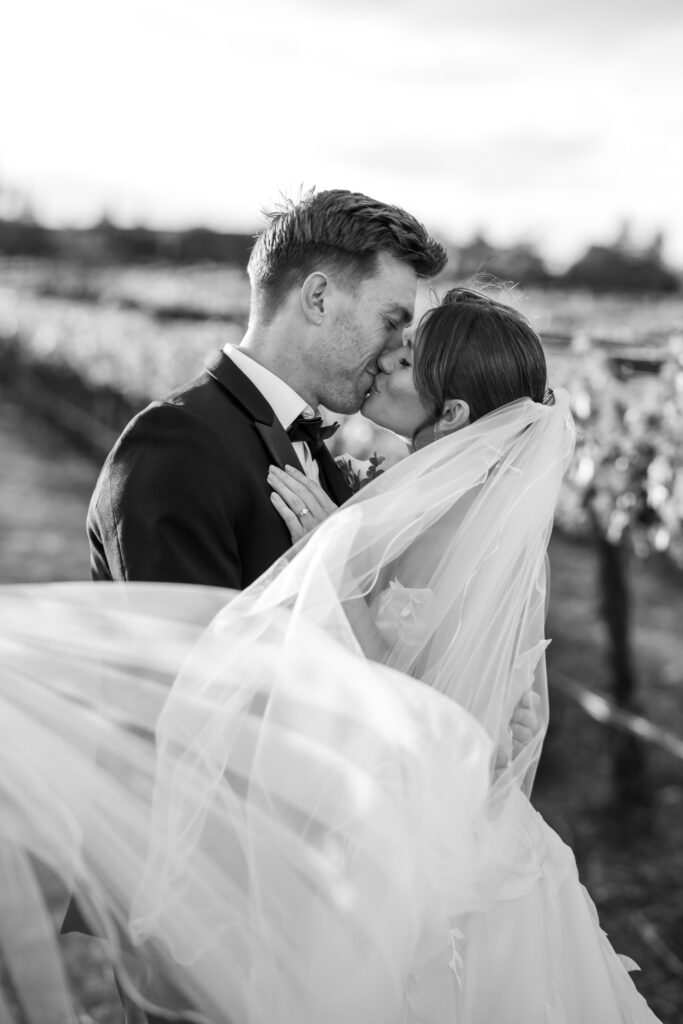 Bride and groom kissing in the Napa Valley vineyard rows with veil flowing, photographed by Alicia Parks Photography, bridal portraits napa